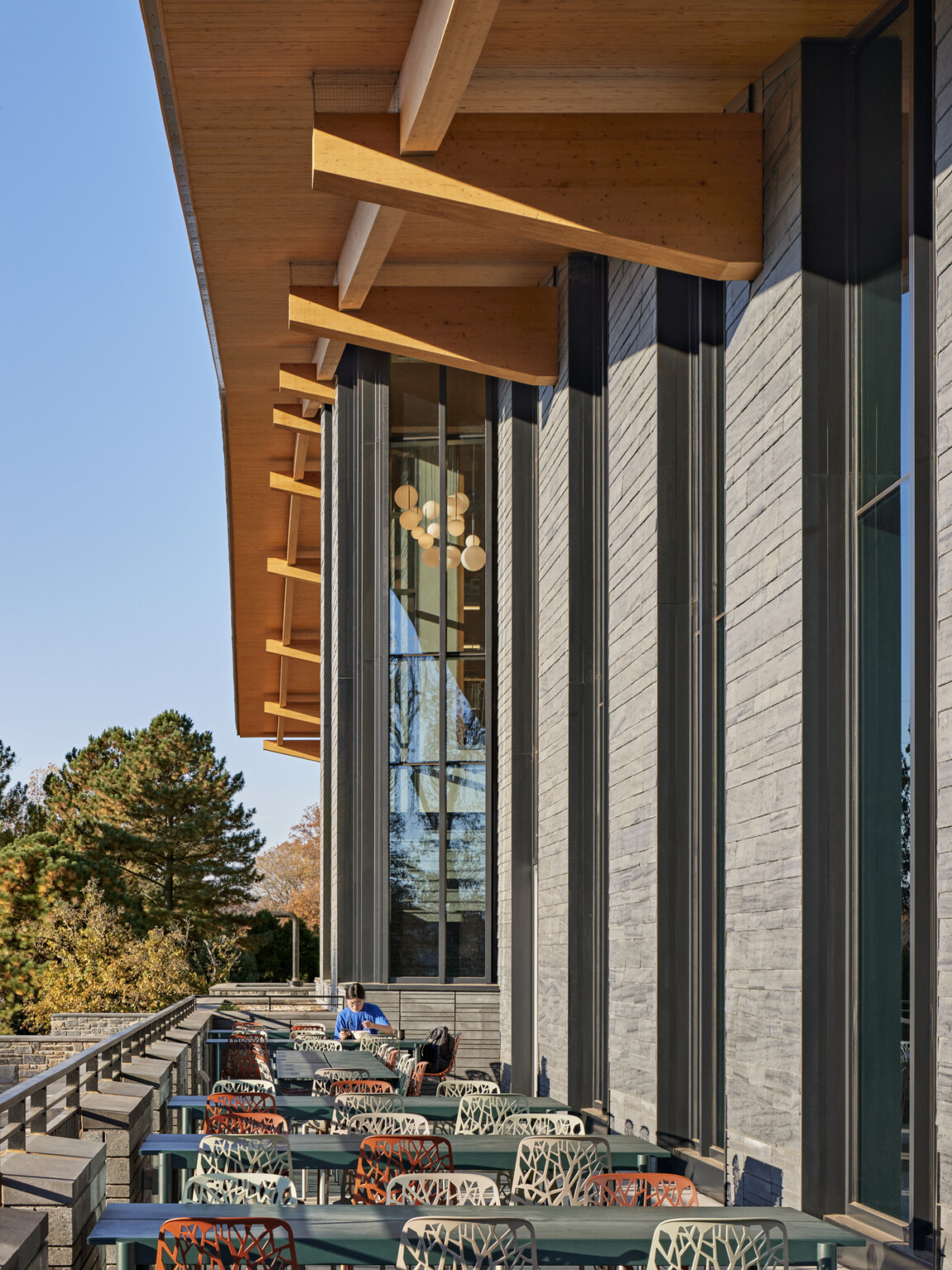 Exterior flexible seating area partially shaded by mass timber canopy overhang on stone building with large windows