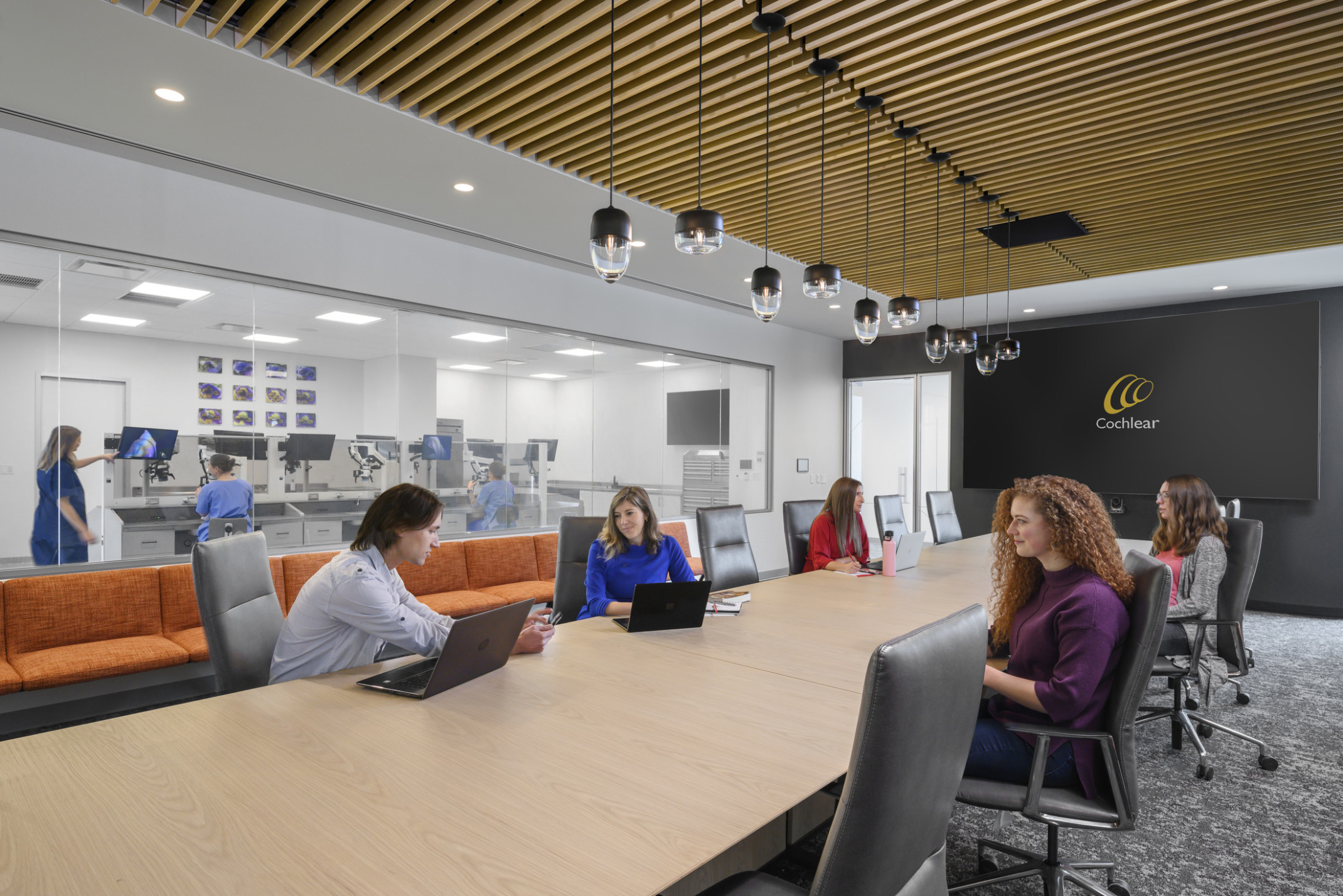 Conference room with wood slat ceiling over long table with pendant lights down center. Black back wall with large screen Conference room with wood slat ceiling over long table with pendant lights down center. Black back wall with large screen
