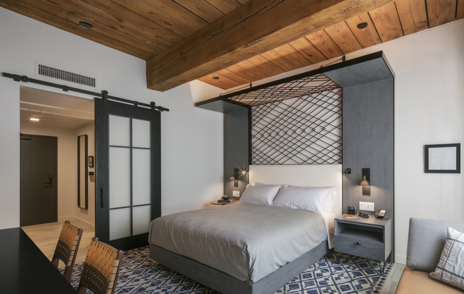hotel guestroom with gray bedding, woven fiber headboard and heavy timber ceiling and beams