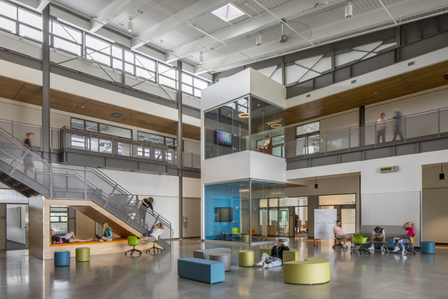 Double height atrium with angled ceiling looking at the corner 2 stacked colorful glass learning pods in front of upper hall Double height atrium with angled ceiling looking at the corner 2 stacked colorful glass learning pods in front of upper hall