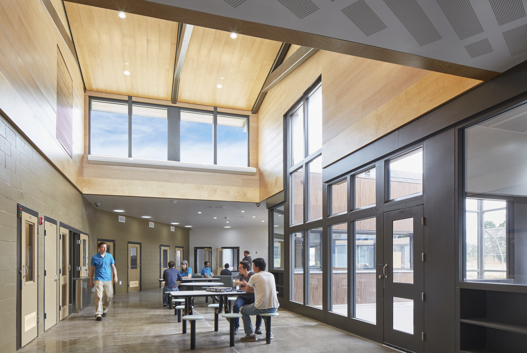 Oregon Youth Authority Maclaren Campus entry hallway. Black framed double height windows at entrance and wood upper walls Oregon Youth Authority Maclaren Campus entry hallway. Black framed double height windows at entrance and wood upper walls