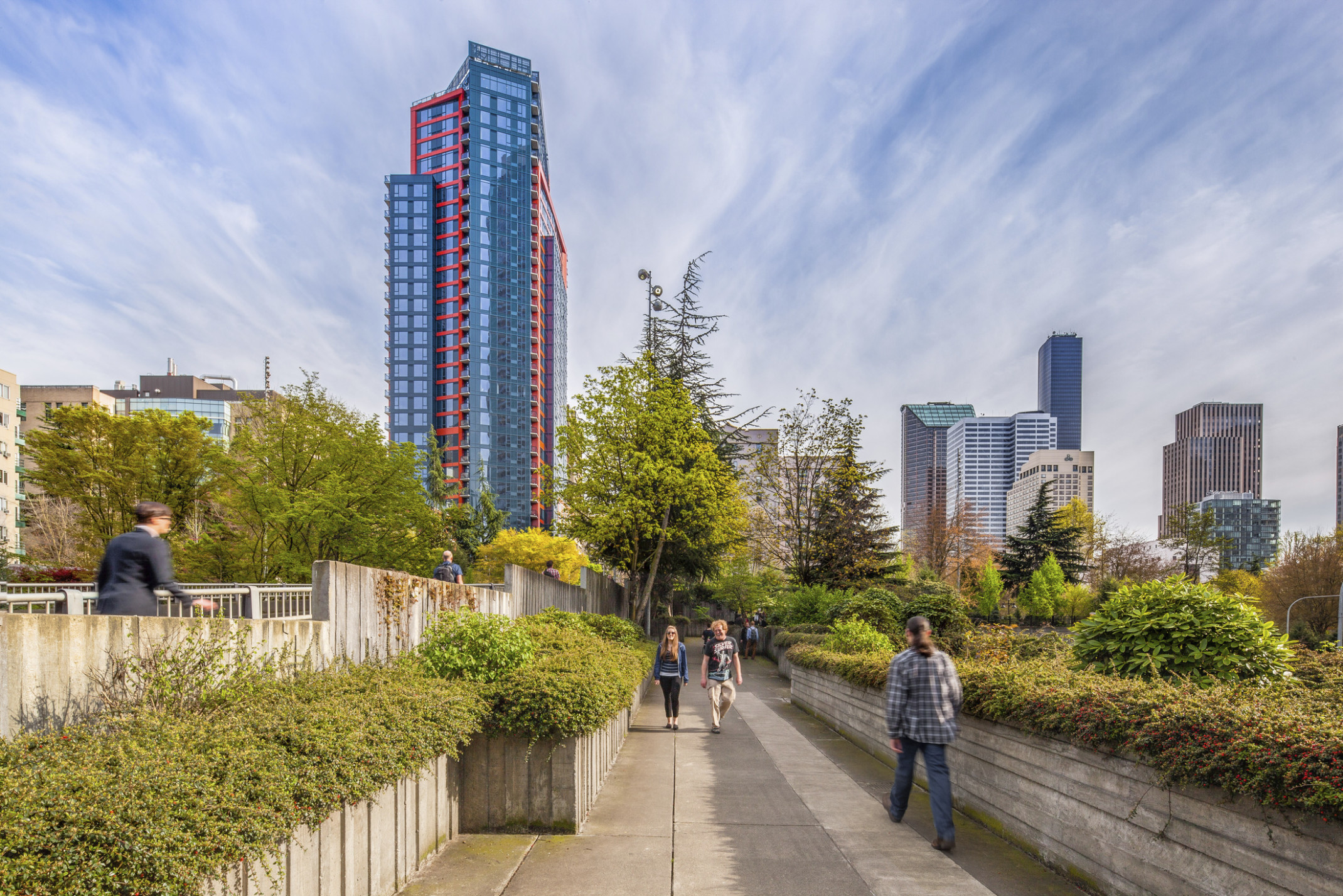 Cielo, a layered glass building with red and blue wrapping facade, behind a tree lined walkway surrounded by skyscrapers Cielo, a layered glass building with red and blue wrapping facade, behind a tree lined walkway surrounded by skyscrapers