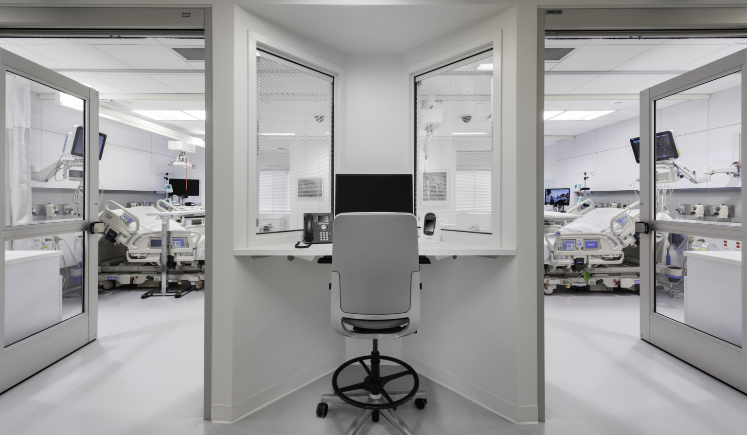 a desk between observation windows looking into two patient rooms a desk between observation windows looking into two patient rooms