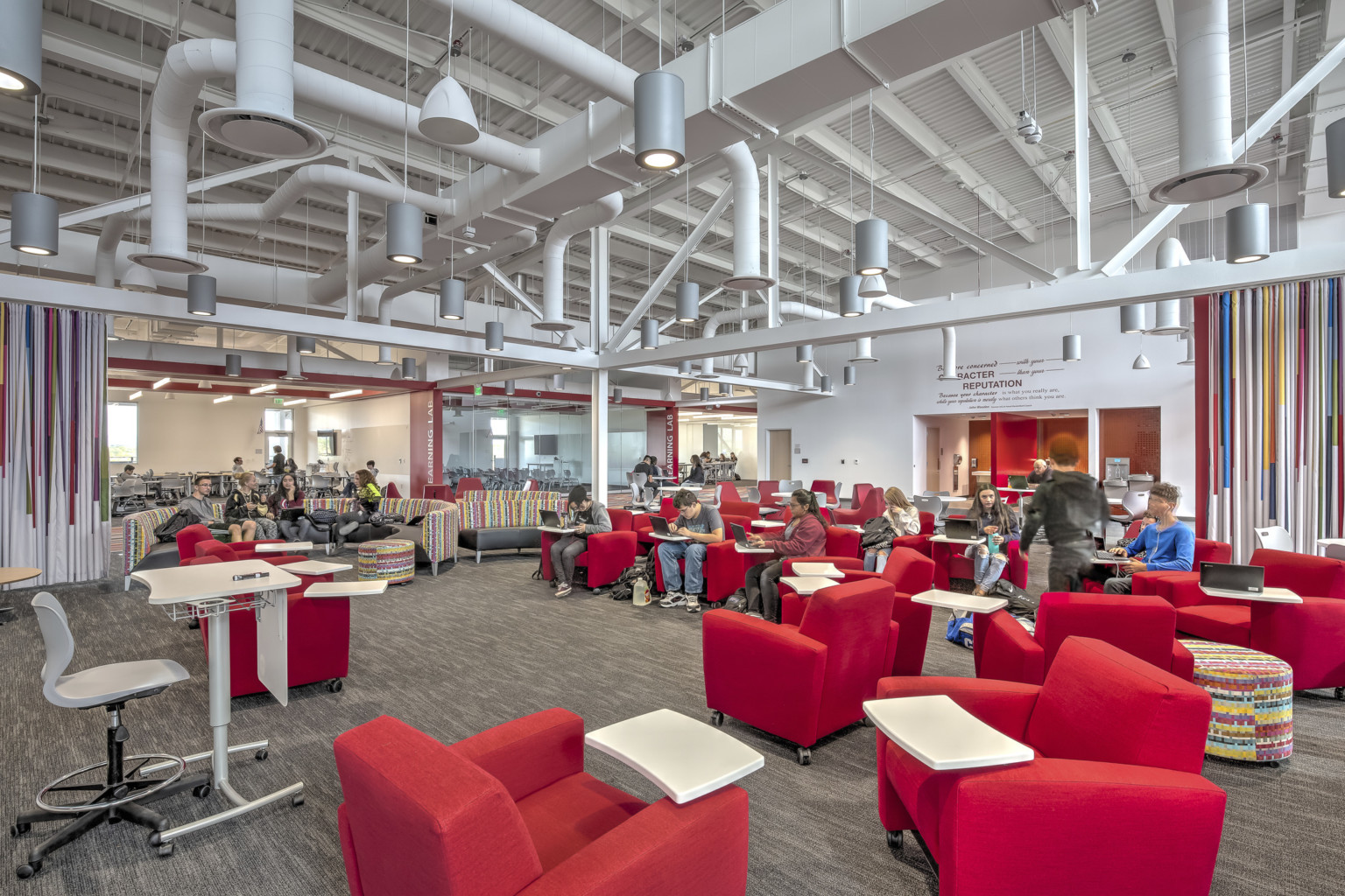 Large carpeted white room with red armchairs. Striped accent walls. Exposed ductwork and hanging pendant lights overhead