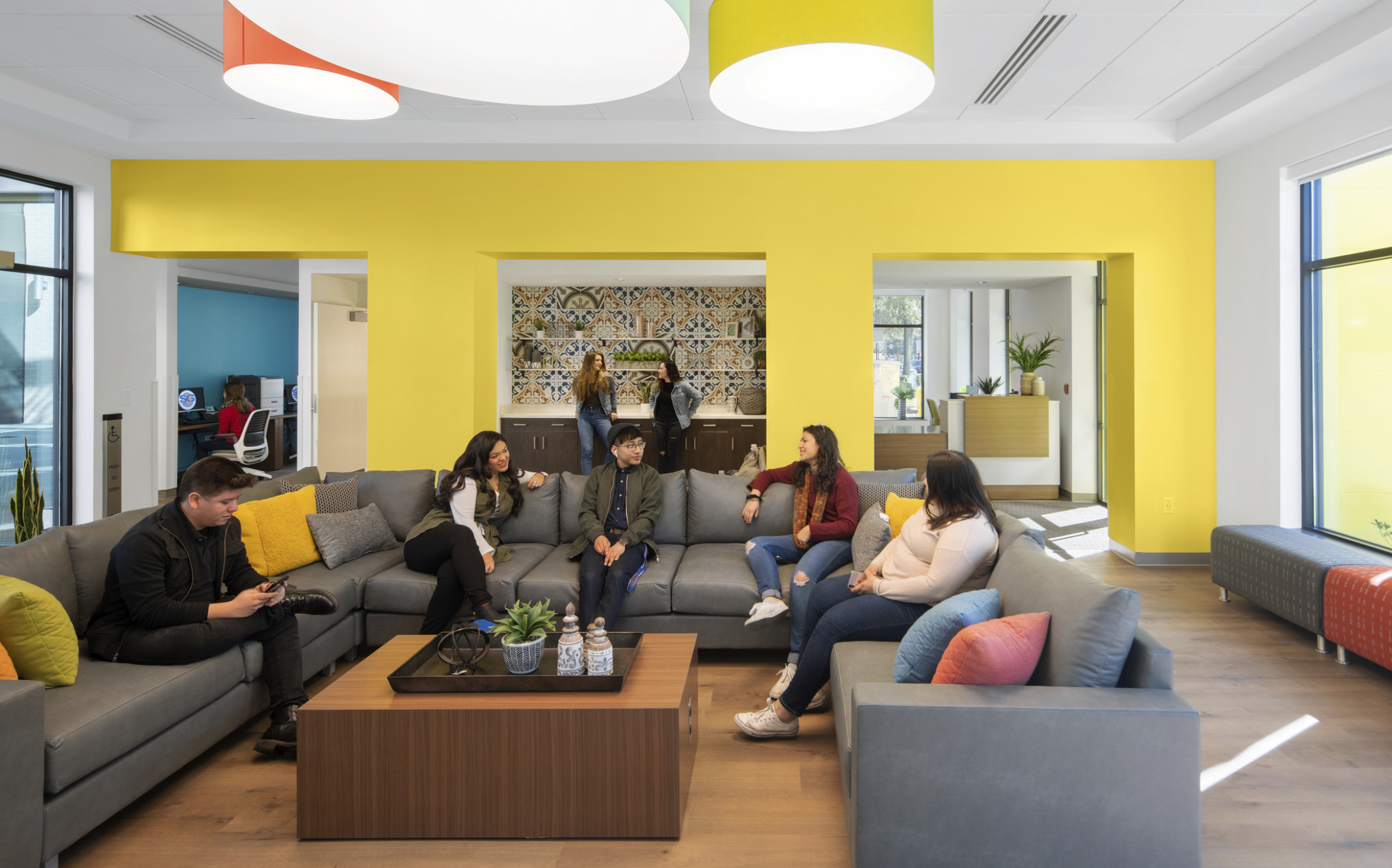 students sitting around a couch with yellow walls and drop pendant lighting for inviting and home away from home environment