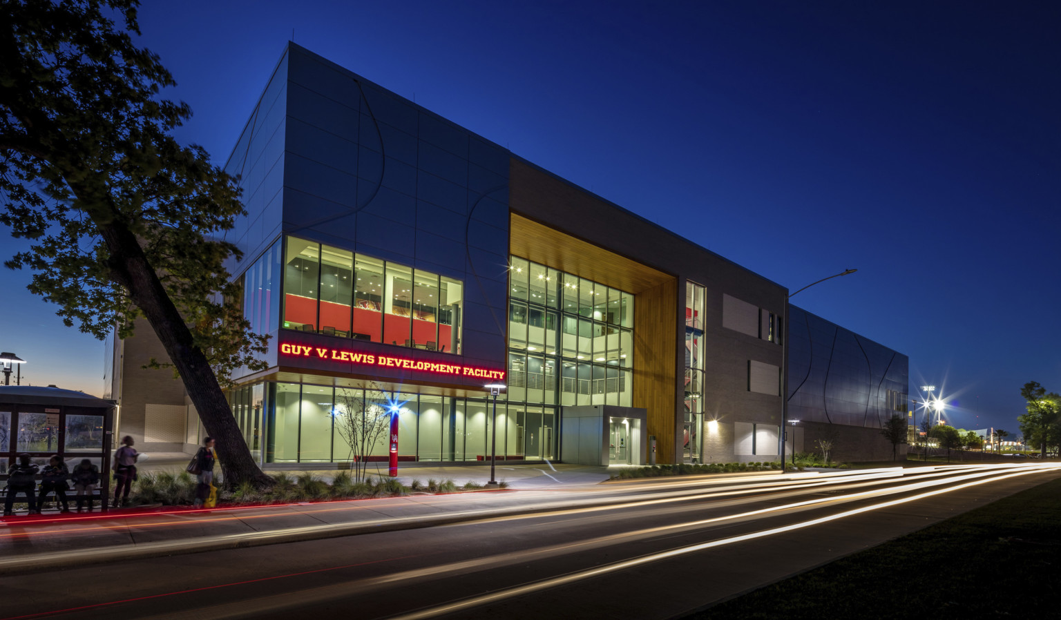 Guy V. Lewis Development Facility illuminated at night with red sign left of triple height glass entrance with wood accent