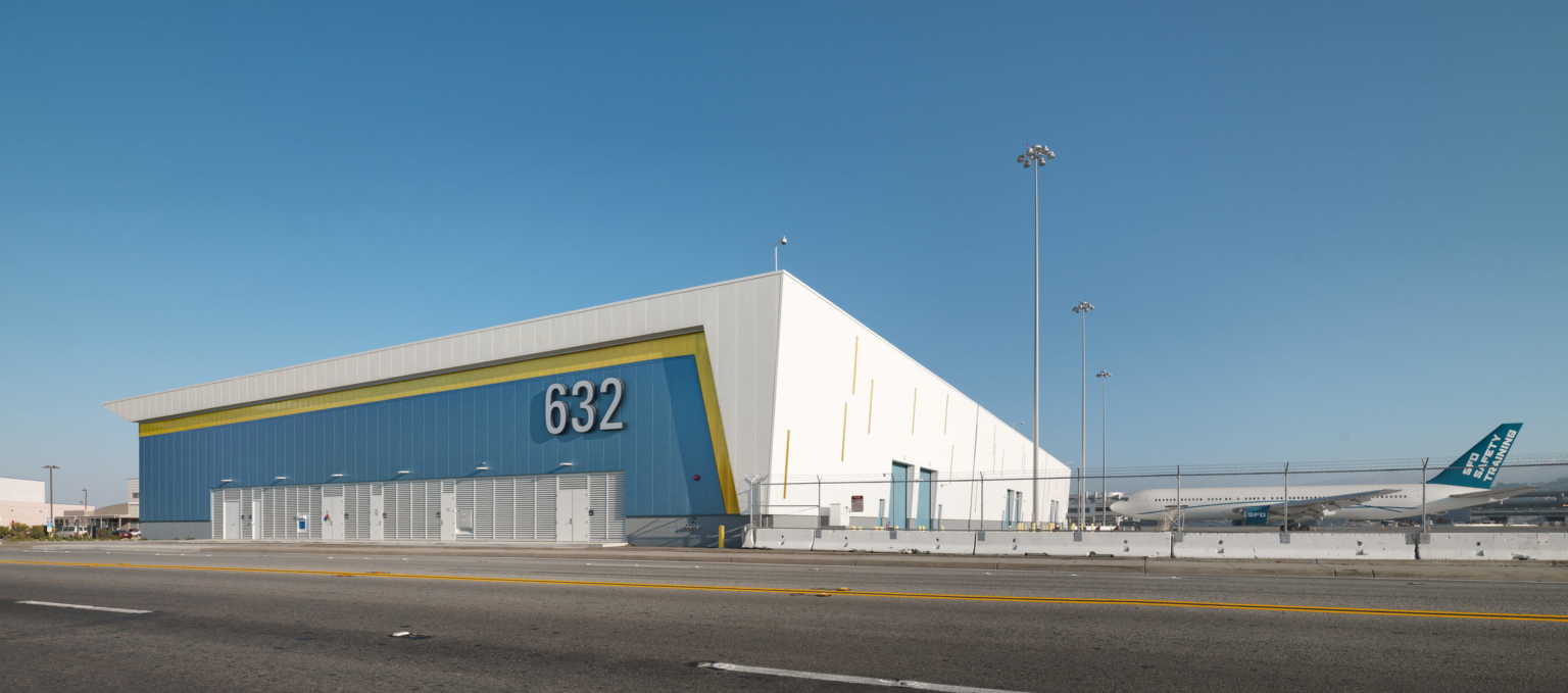 exterior view of blue yellow and white cargo building at airfield with airplane and blue sky