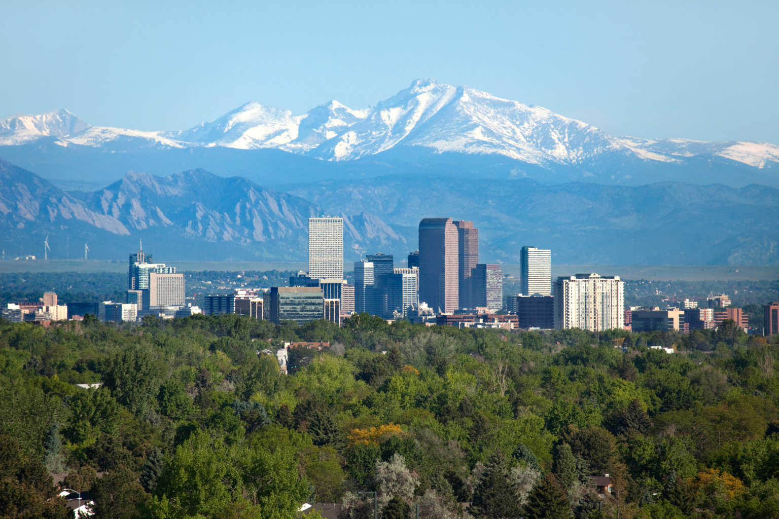 the denver skyline with greenspace in the foreground and the snowcapped rocky mountains in the background