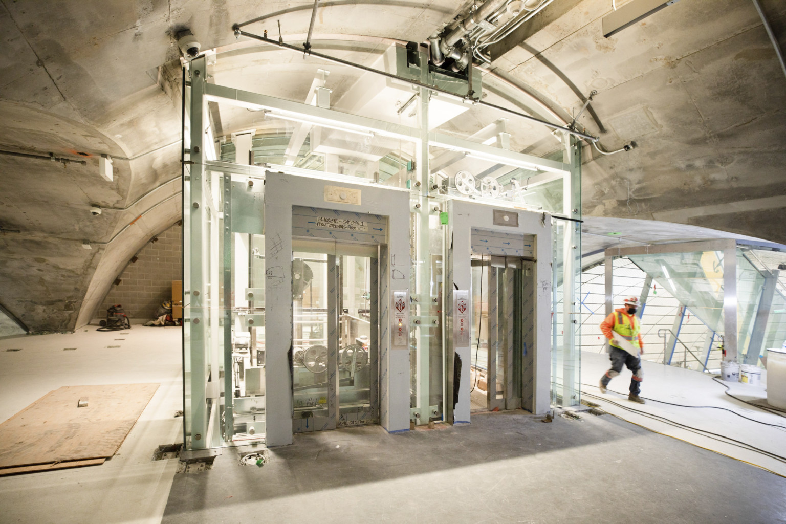 Domed upper level tunnel with stairs, back right, behind elevator shaft under construction. Raw concrete ceiling and floor