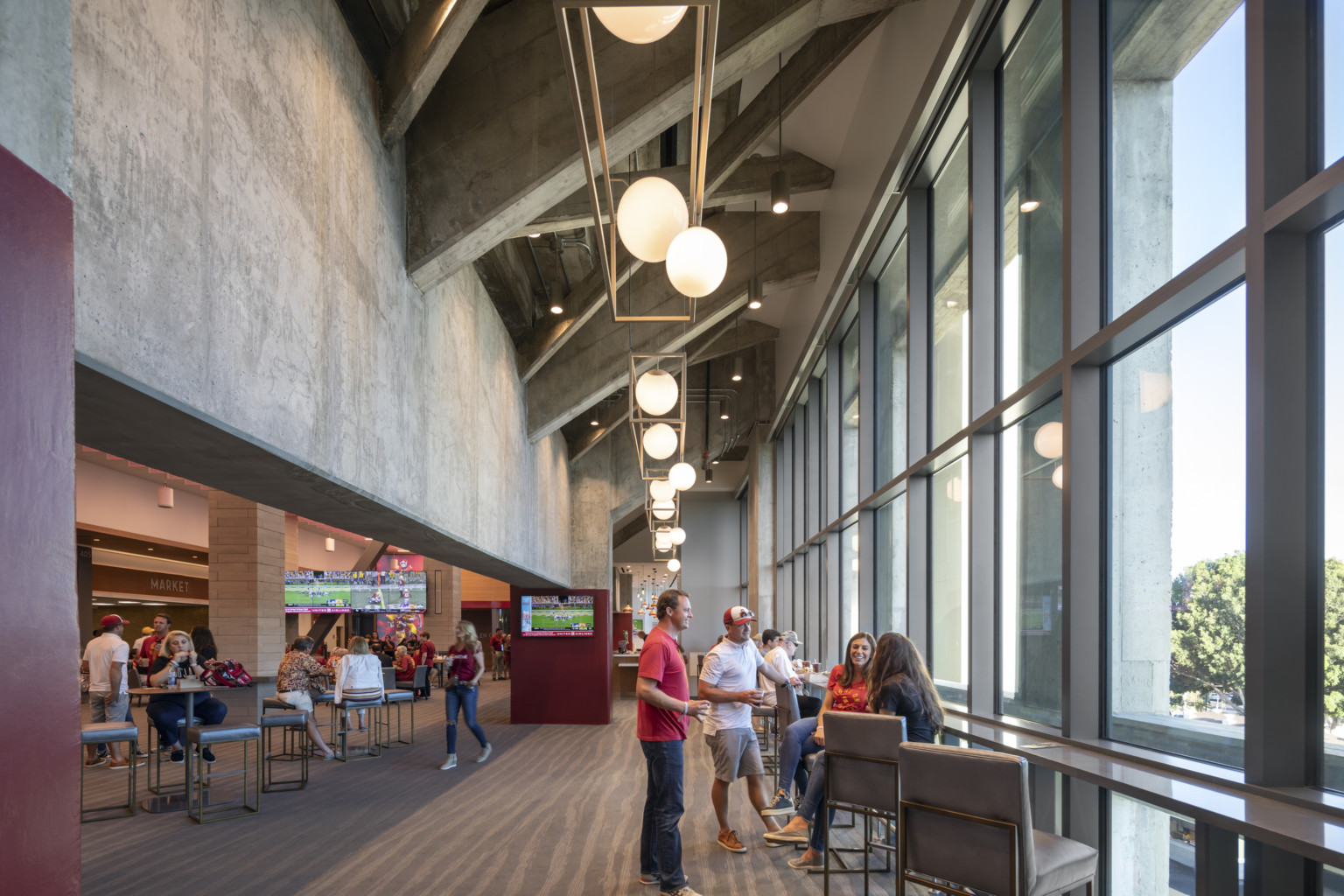 Raw concrete from stadium forms drop ceiling detail left of counter along floor to ceiling windows. Center, pendant lights
