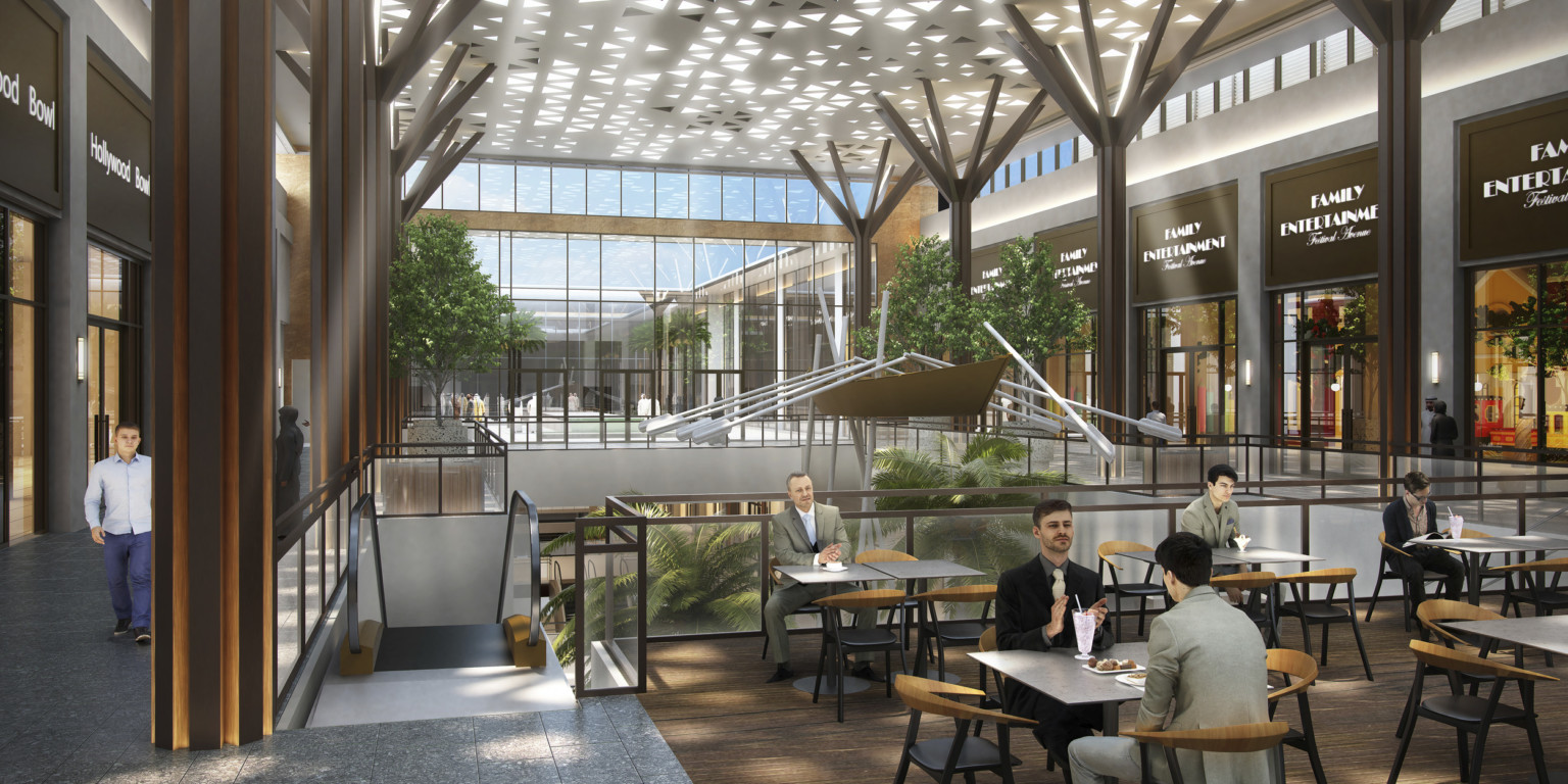 Seating area in atrium upper level. Shops along sides with double height glass wall, back. Panel with triangle cutouts above