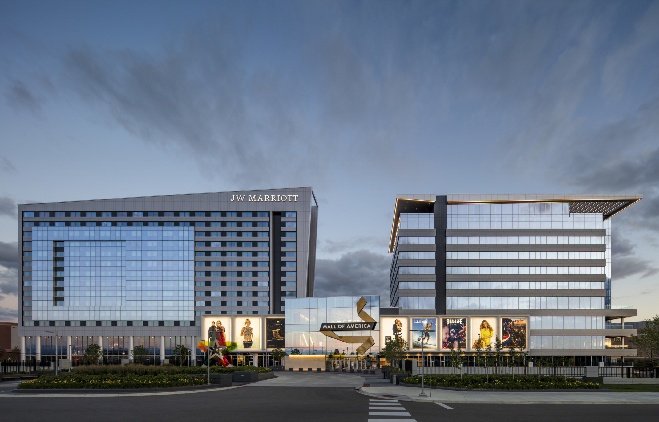 Mall of America entry with illuminated signage connecting 2 grey angled buildings. Left building labelled JW Marriott Mall of America entry with illuminated signage connecting 2 grey angled buildings. Left building labelled JW Marriott