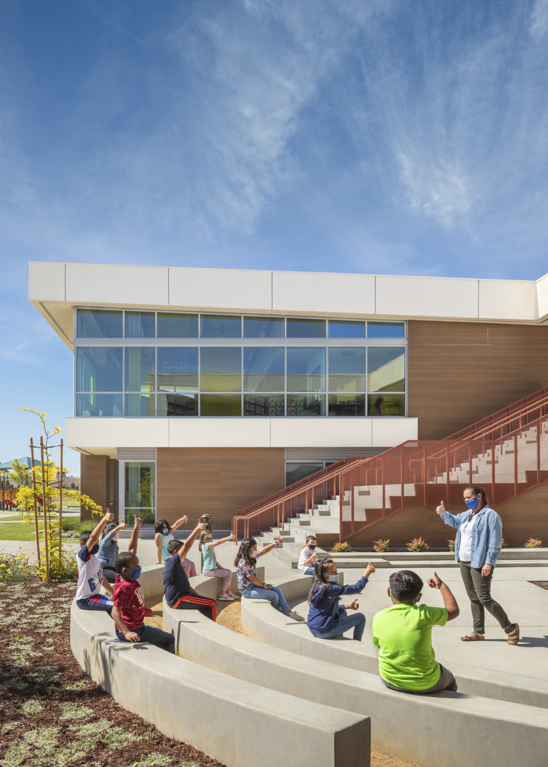 Rounded concrete bench seats facing to school. Behind are stairs with orange railing in front of brown and white building