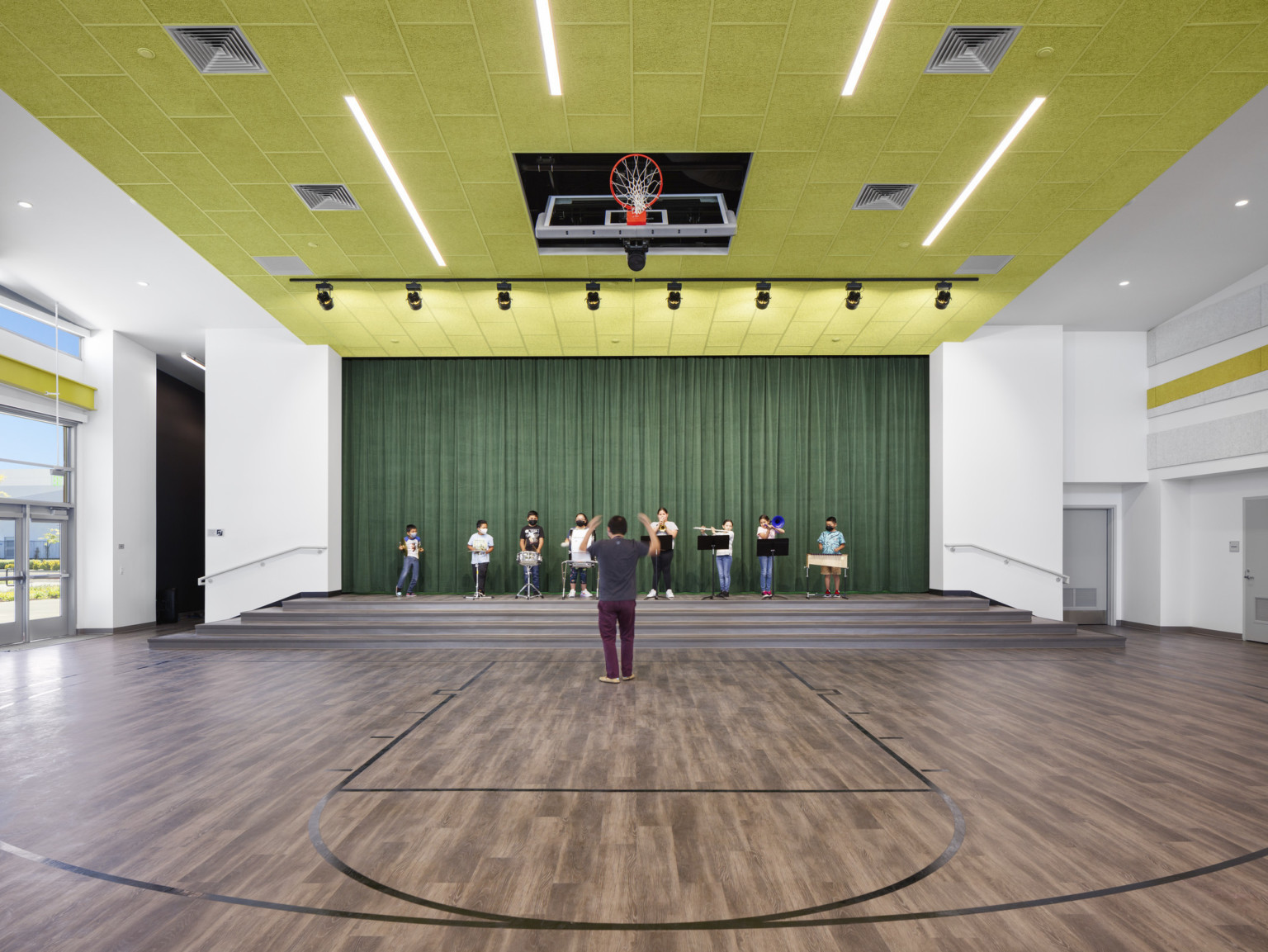 Interior gymnasium with stage in use. Green ceiling and stage curtains. Basketball hoop lifts into ceiling for performance
