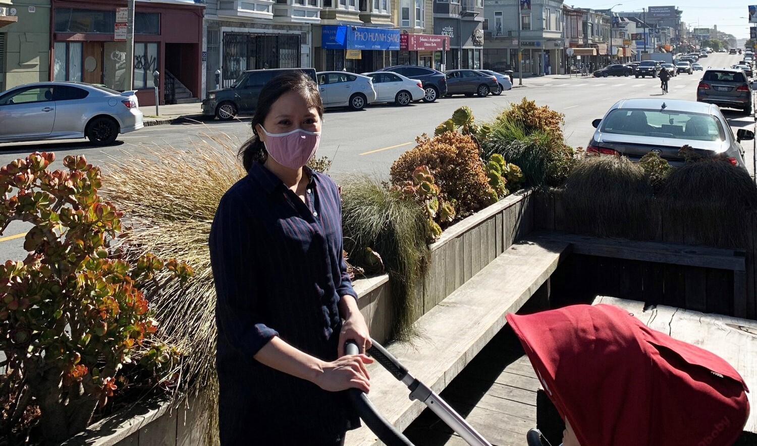 Catherine Meng pushing a red hooded stroller in an outdoor seating area on a street with row buidlings Catherine Meng pushing a red hooded stroller in an outdoor seating area on a street with row buidlings