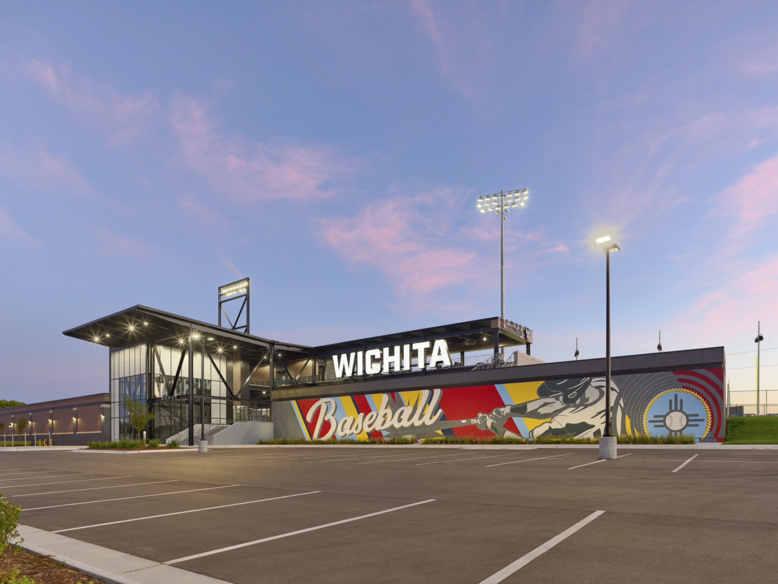 Illuminated Wichita Sign on 2nd floor above baseball mural, right of stadium entrance. Canopy over entry and roof patio right