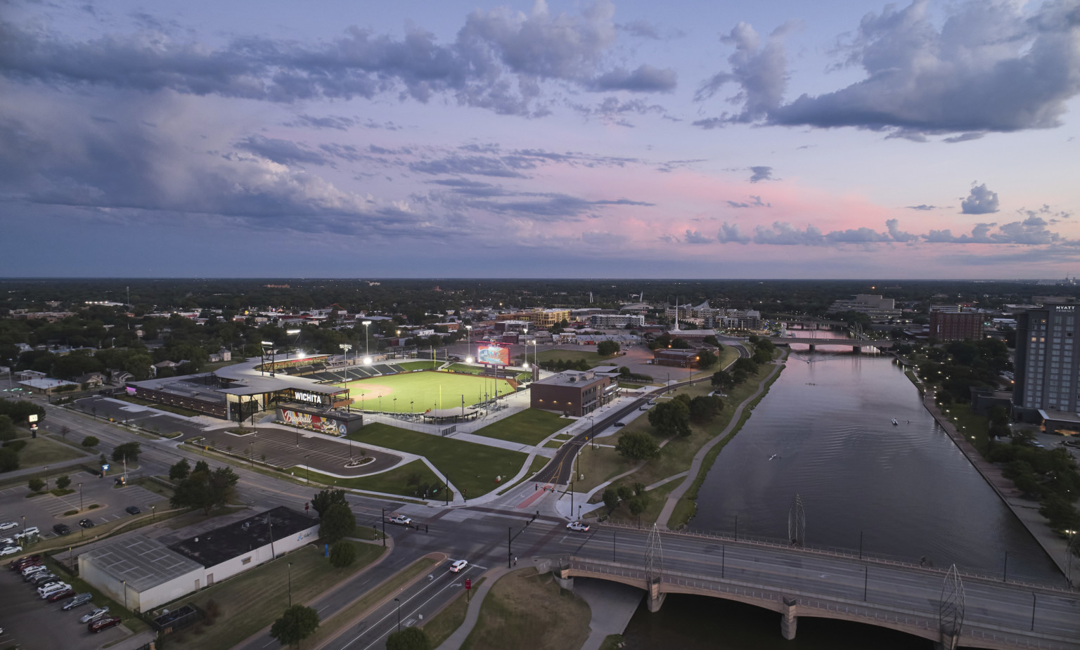 Corner view of the stadium from above the Arkansas River. Baseball field is illuminated with stadium lights