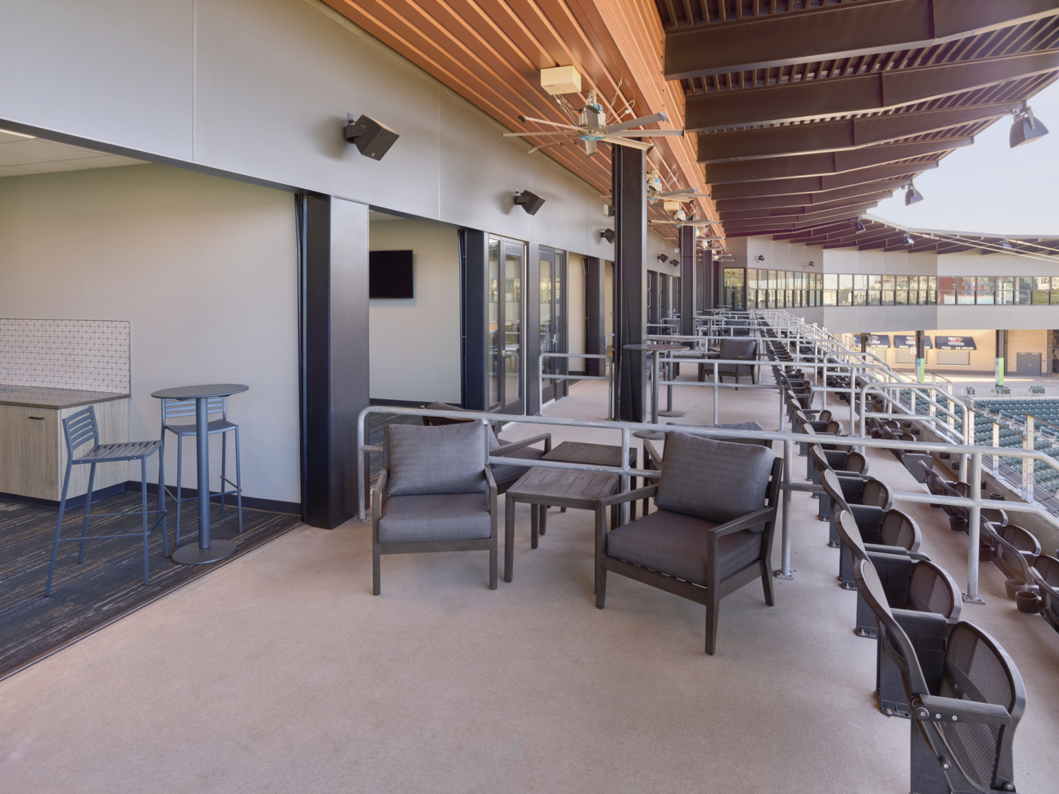 Suites on left with flexible wall opened out to patio with padded chairs and stadium seating. Grey railings between suites