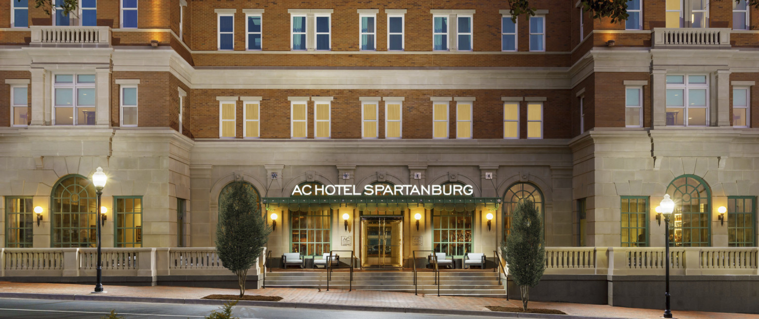 Exterior of hotel entry with sign illuminated on green awning. Green arches windows on carved front stone wall Exterior of hotel entry with sign illuminated on green awning. Green arches windows on carved front stone wall