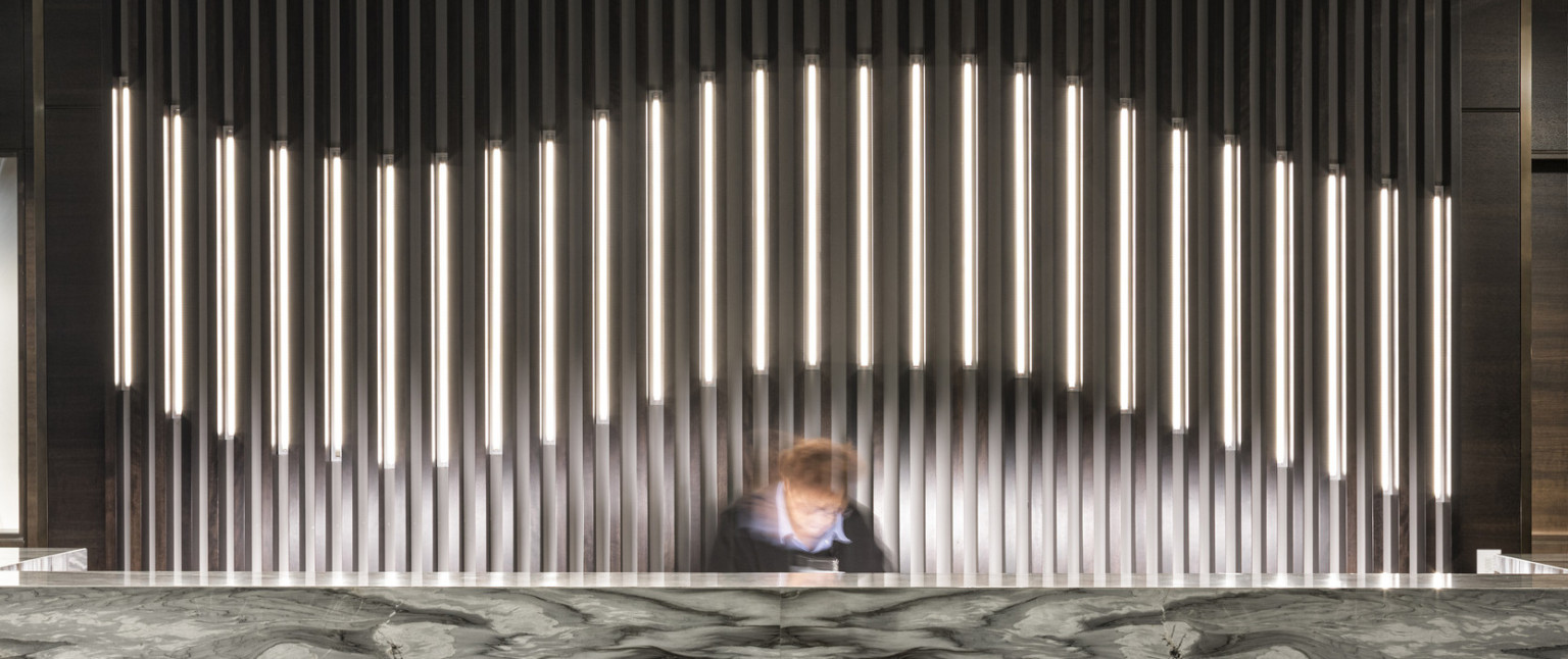Dark marbled reception desk in lobby with thin pillared wall details, partially illuminated curve along center