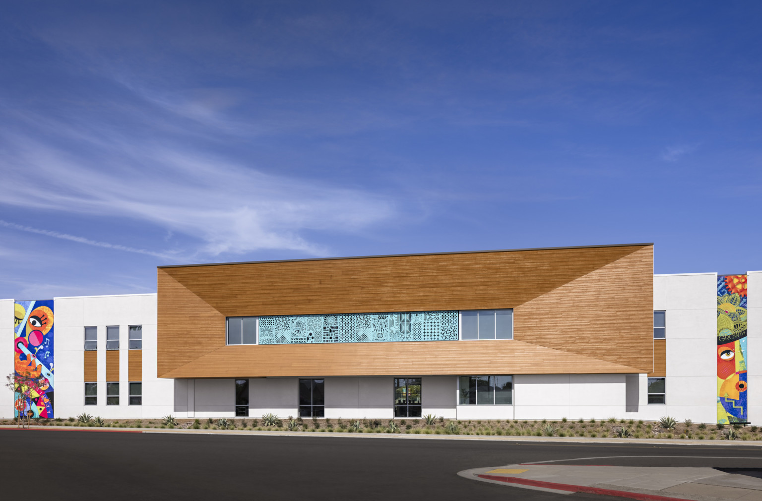 Exterior of white back wall with wood box extension at center, angled toward windows with translucent panels. Murals on sides Exterior of white back wall with wood box extension at center, angled toward windows with translucent panels. Murals on sides