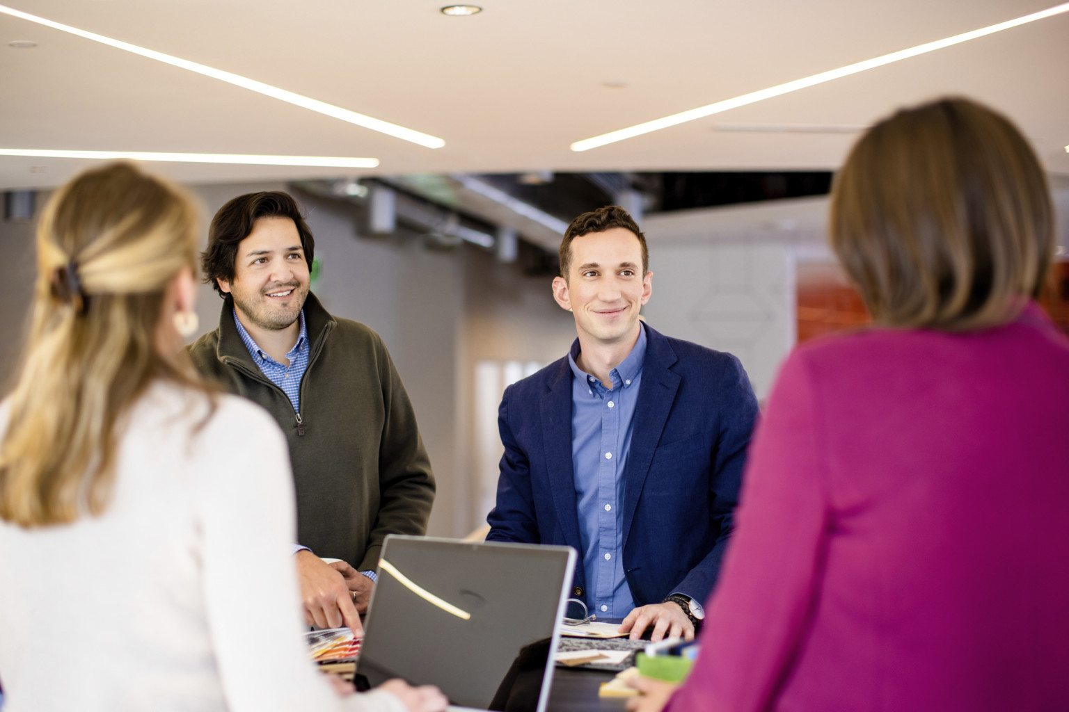 a group of smiling young professionals collaborating around a standing height table under a ceiling with diagonal lighting a group of smiling young professionals collaborating around a standing height table under a ceiling with diagonal lighting