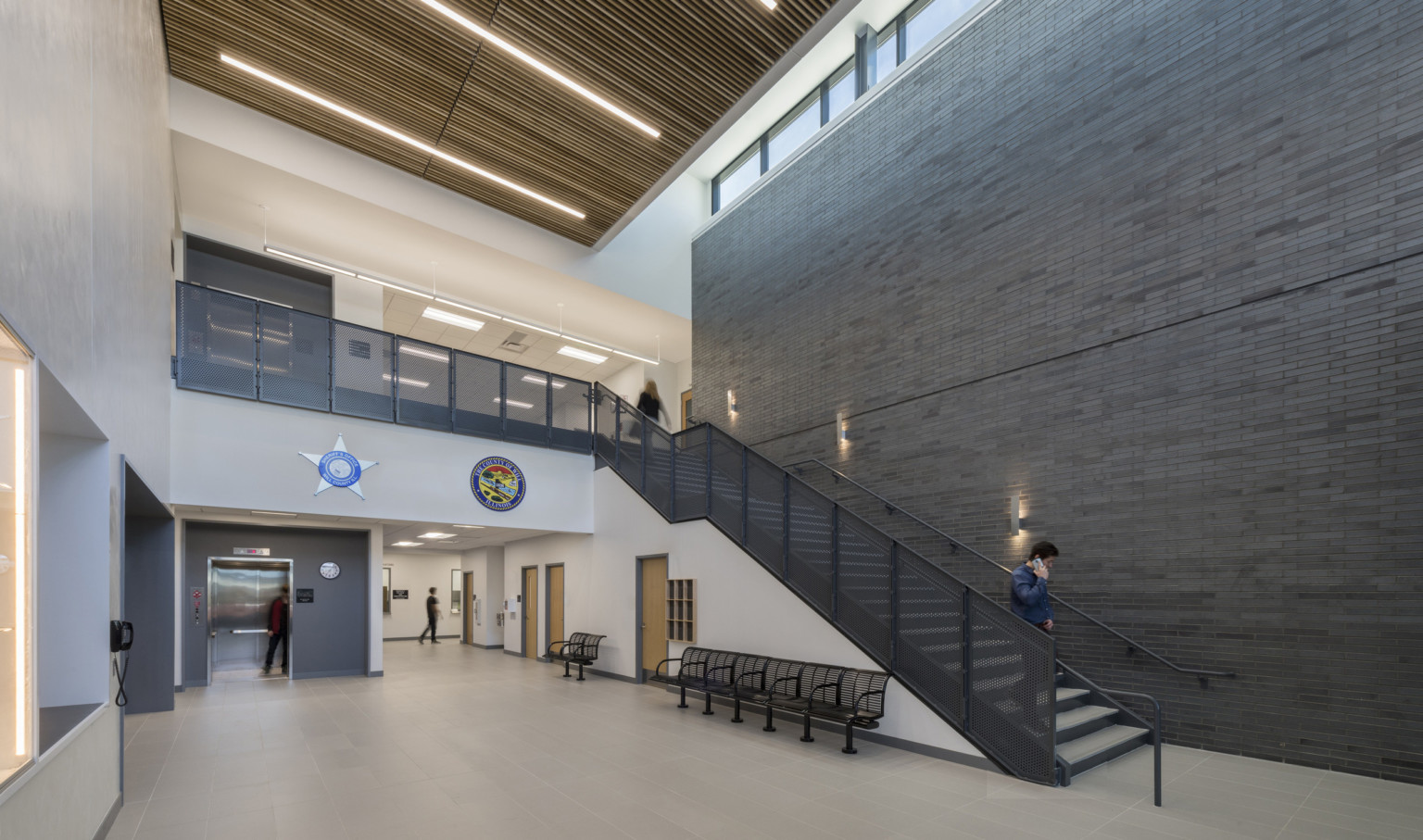 Double height atrium inside Will County Public Safety Center, grey and white walls and a dark staircase with scone lighting