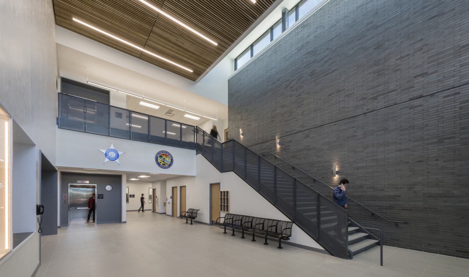 Double height atrium inside Will County Public Safety Center, grey and white walls and a dark staircase with scone lighting Double height atrium inside Will County Public Safety Center, grey and white walls and a dark staircase with scone lighting