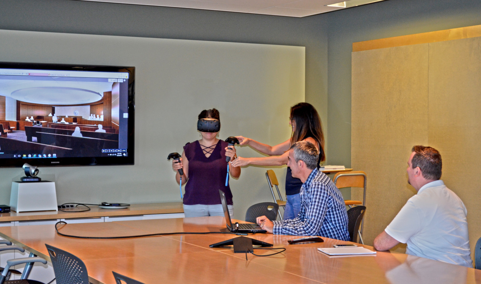 people around a table where woman is using virtual reality system to experience mock-up of courtroom design