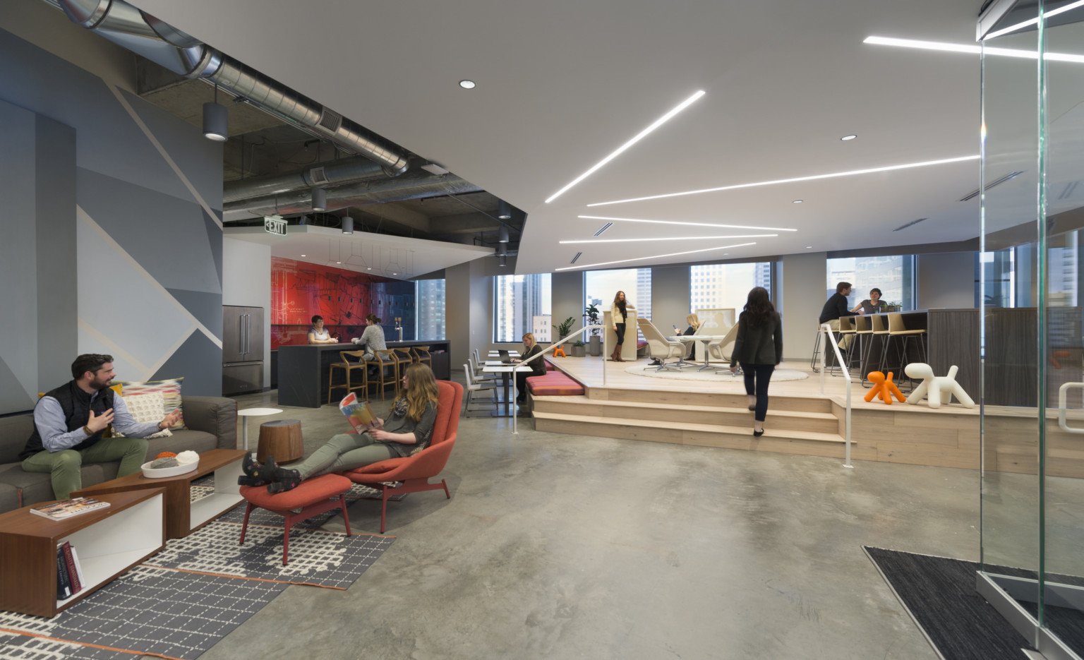 people conversing in clusters in an open office with a raised stage platform seating area, a custom bench seating and glass enclosed conference room people conversing in clusters in an open office with a raised stage platform seating area, a custom bench seating and glass enclosed conference room