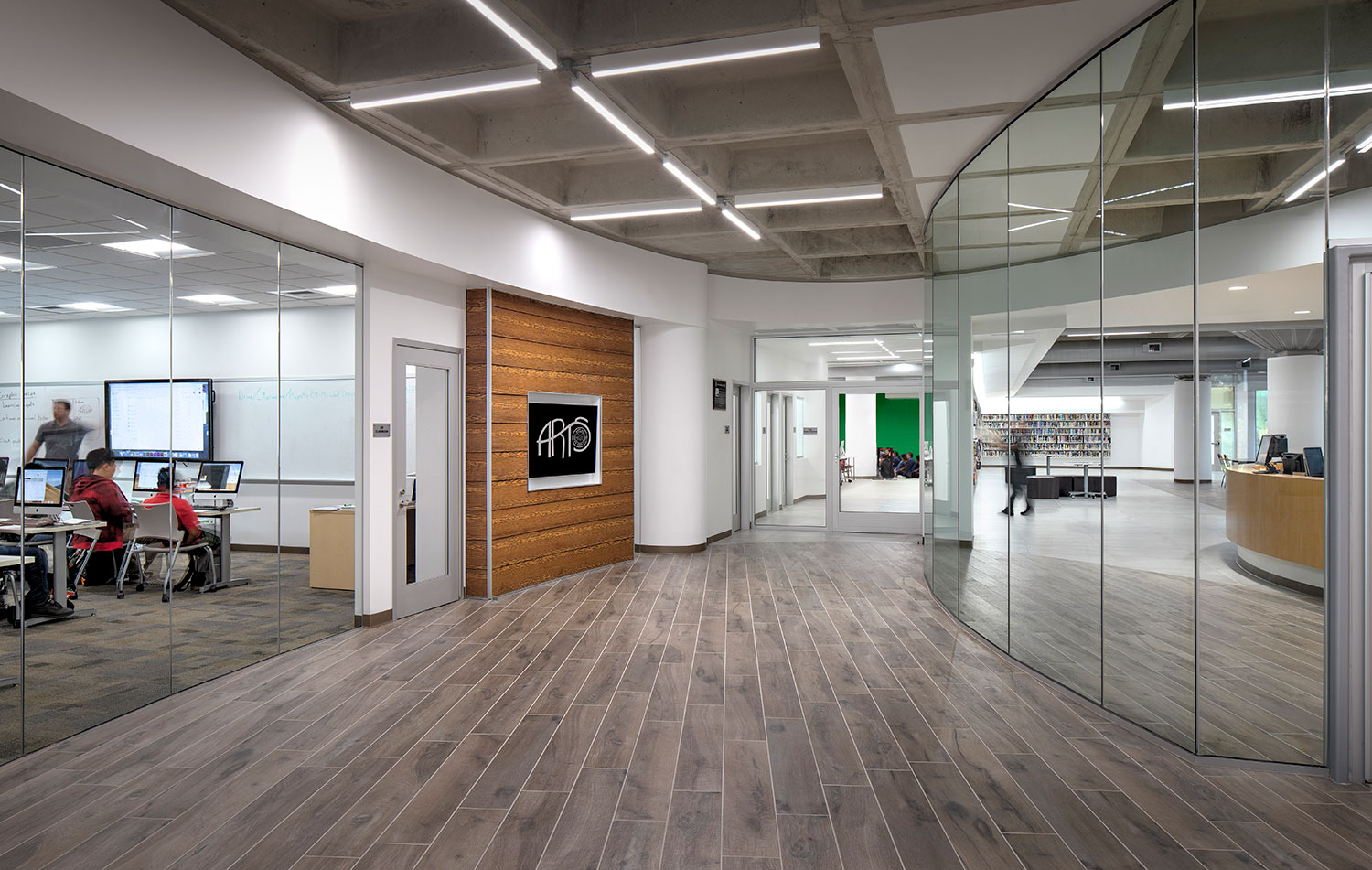 waffle slab ceiling with orthogonal lighting and wooden floor in a hallway lined with glass walled media labs and classrooms