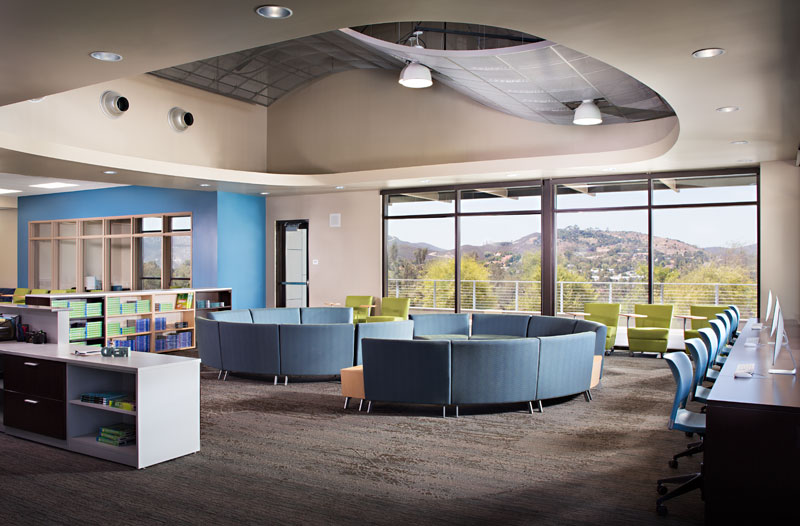 oval ceiling recess above circular blue lounge seating in library learning area with blue and beige and tall glass walls