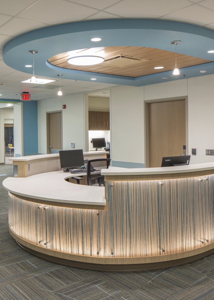 Semi circular reception desk with textural illuminated overlay. Light blue and wood dropped ceiling detail mirrors desk shape