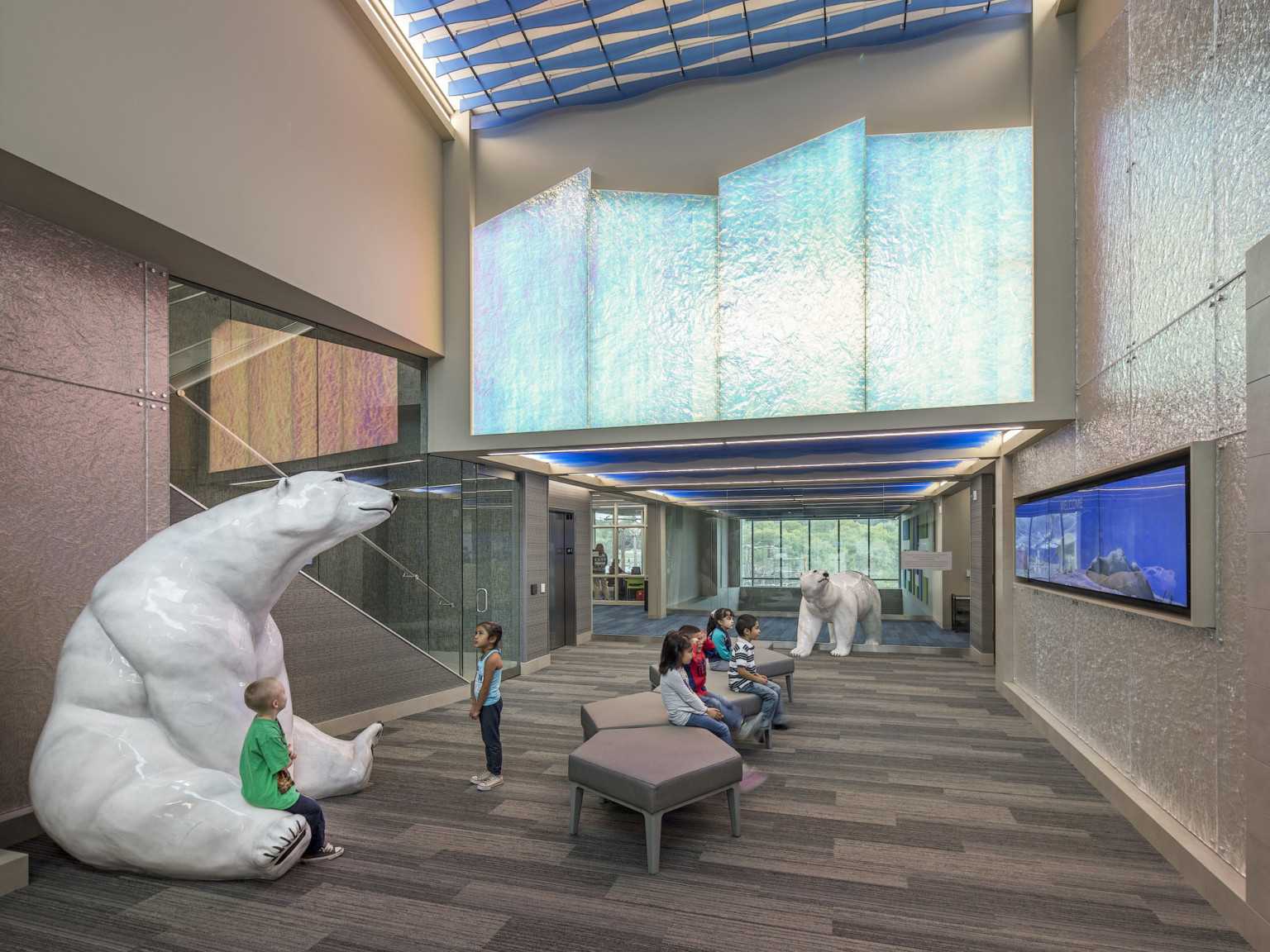 Large polar bear sculptures in a double height to drop ceiling hallway. In drop wall are 4 ice like iridescent angled panels