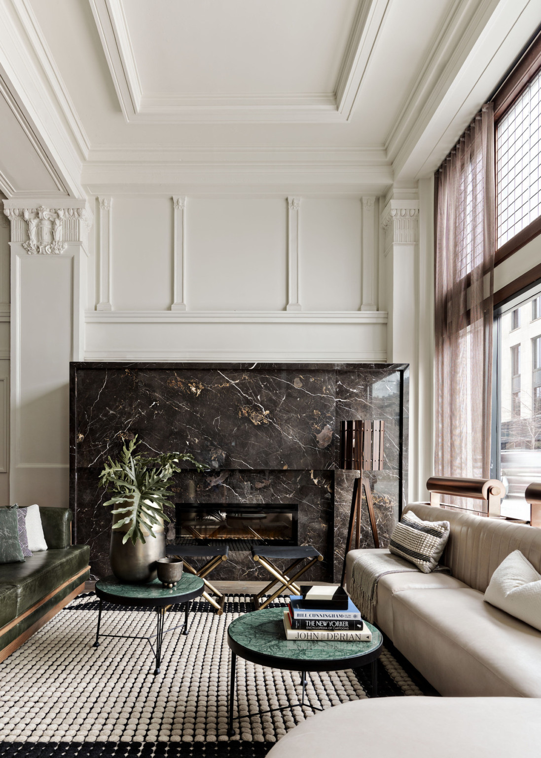 Seating area with arm chairs and cushioned bench along windows. Dark marbled fireplace on white wall with pillars and molding