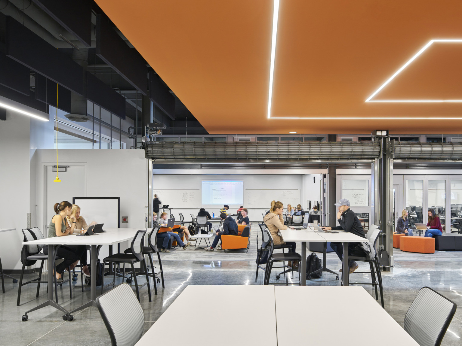 Large commons space with seating under a black ceiling and a geometric orange drop ceiling detail with recessed lights