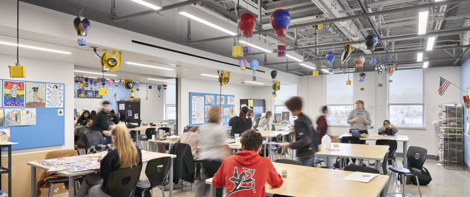 Classroom with exposed structural beams and power cords hanging from ceiling, left. Miniature hot air balloons float above