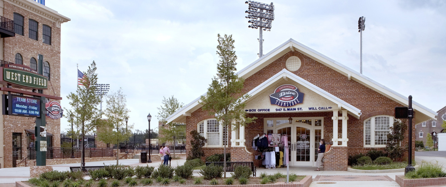 Brick building with pointed roof and entry canopy house team store in stadium plaza with benches and greenery