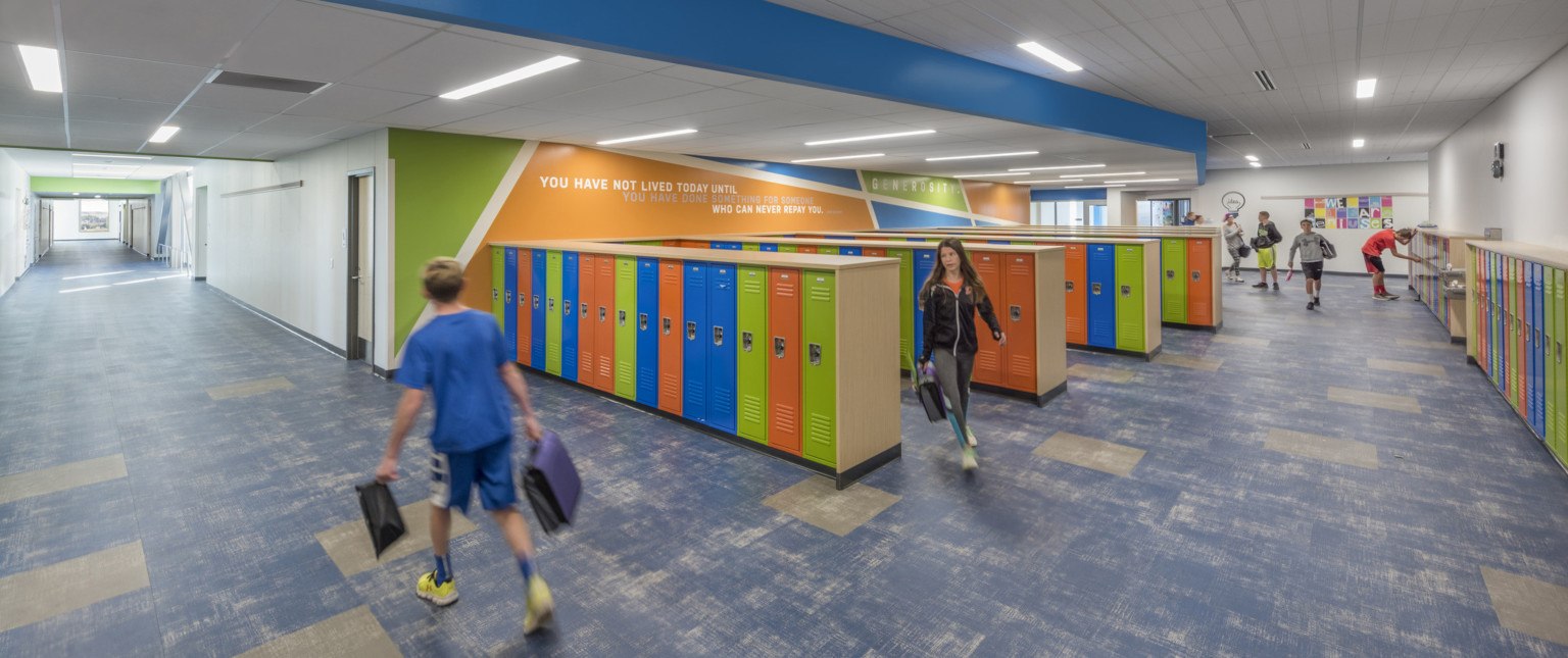 Hall height multicolor lockers in rows and along wall of room with brightly colored geometric mural with quote on left wall