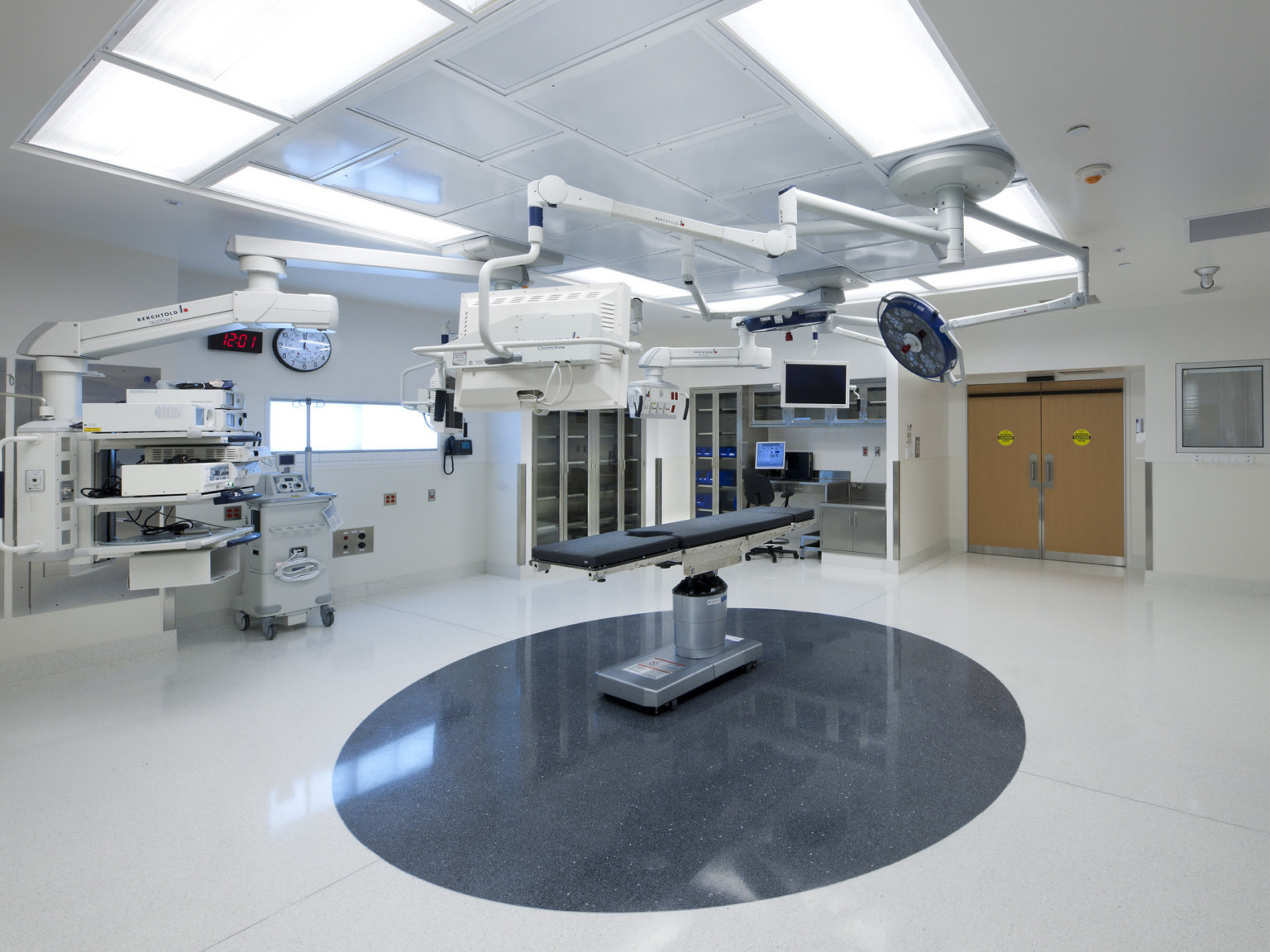 Operating room with table centered over tiled circle in floor. Screens and large circular light fixture suspended from above