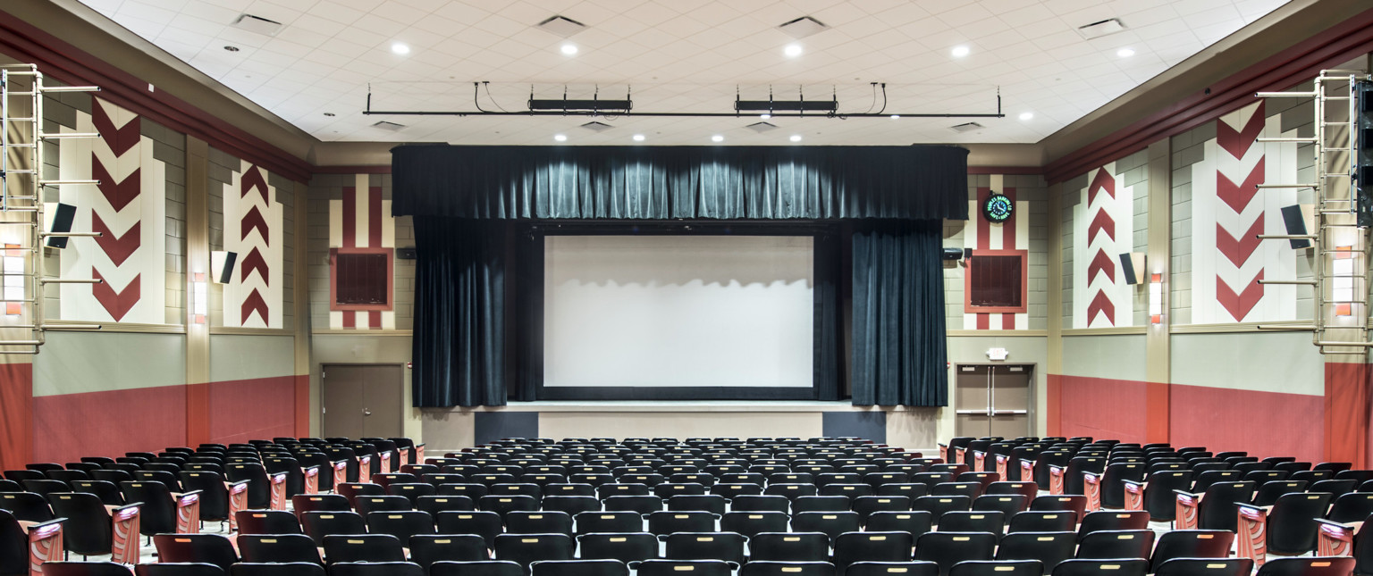 Theater with red band on wall below geometric red and white tiles. Dark blue curtains around screen match with seat backs