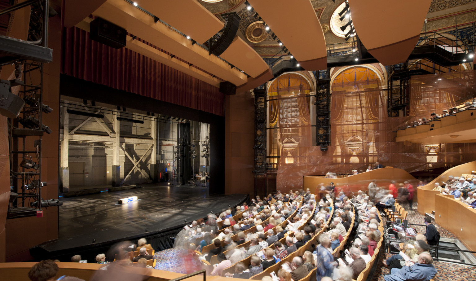 Theater seen from the side over the audience with large arch shaped windows. The stage is empty and stage right can be seen