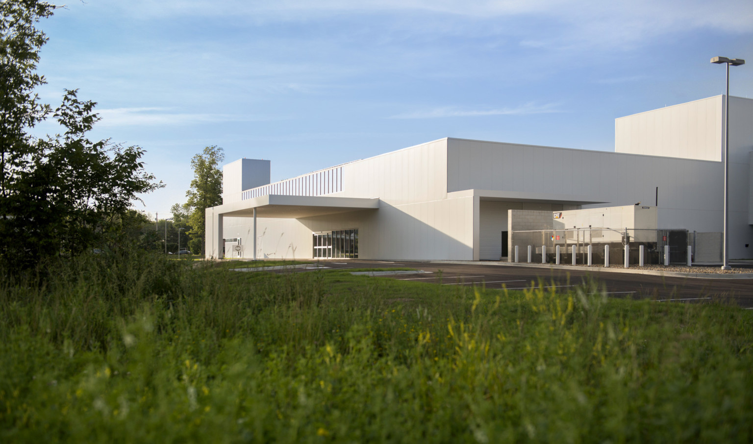 grass and trees in foreground of white modern angular building side entrance with sliding glass doors covered by white canopy grass and trees in foreground of white modern angular building side entrance with sliding glass doors covered by white canopy