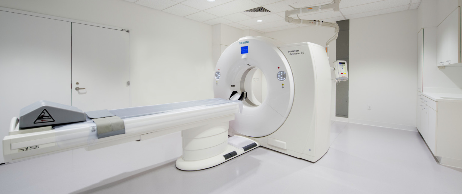 MRI machine at center of white room viewed from the corner near the foot