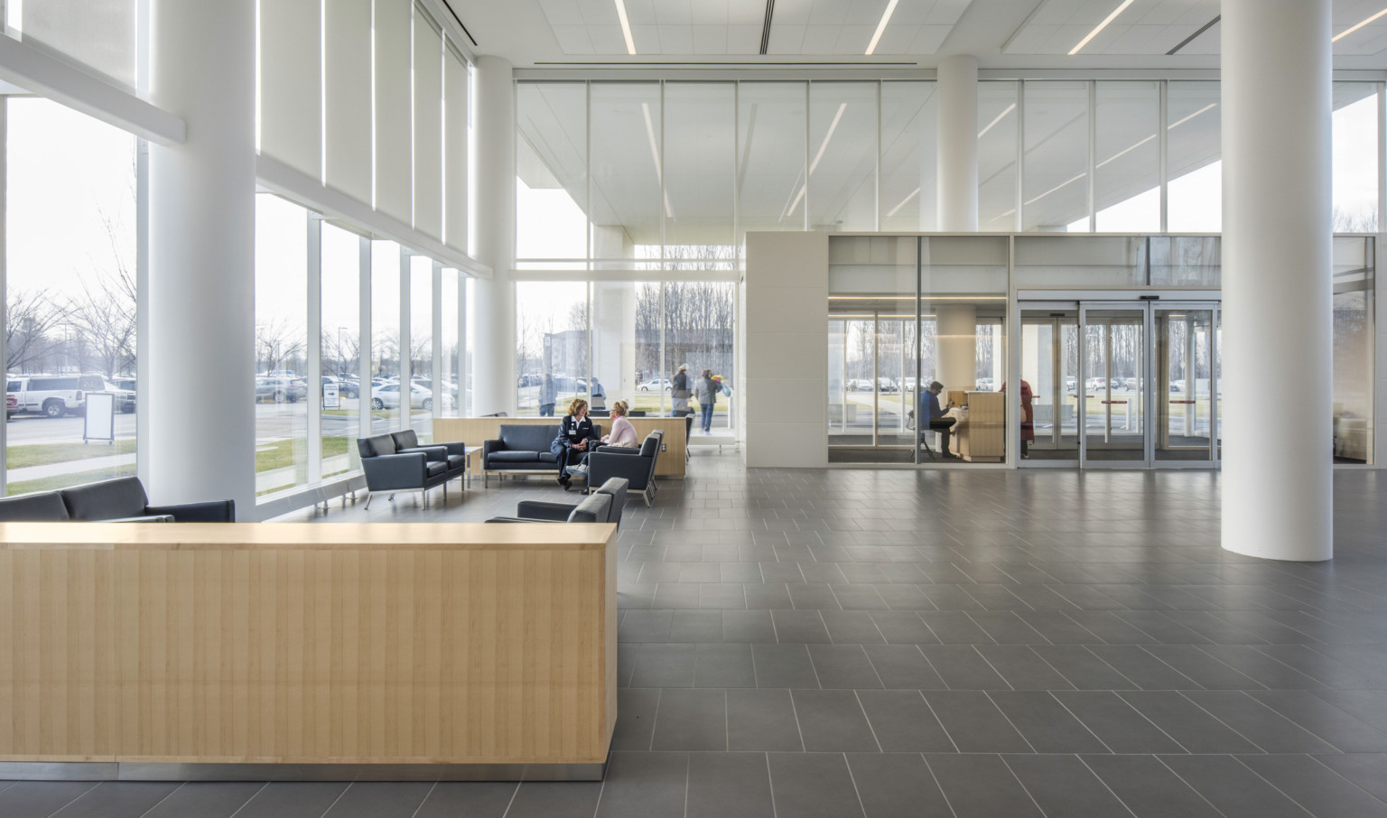 Lobby with double height windows and glass antechamber. Seating area is to the left with couches in a white room with pillars Lobby with double height windows and glass antechamber. Seating area is to the left with couches in a white room with pillars