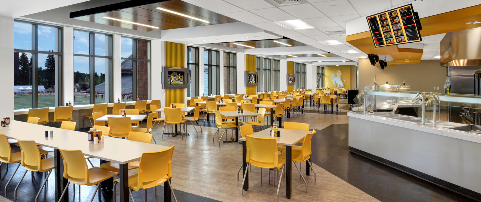 Nutrition Center dining space with tables by floor to ceiling windows, left, looking to field. Cafeteria counter right