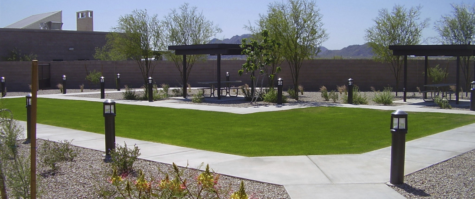 View of courtyard away from building with sidewalk around grassy area near picnic table under shelter with view of mountain