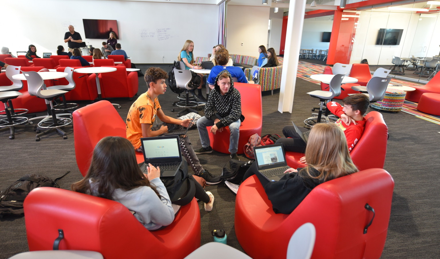 students sitting in a circle in ergonomic red chairs in flexible learning space off hallway with glass walls and red accents