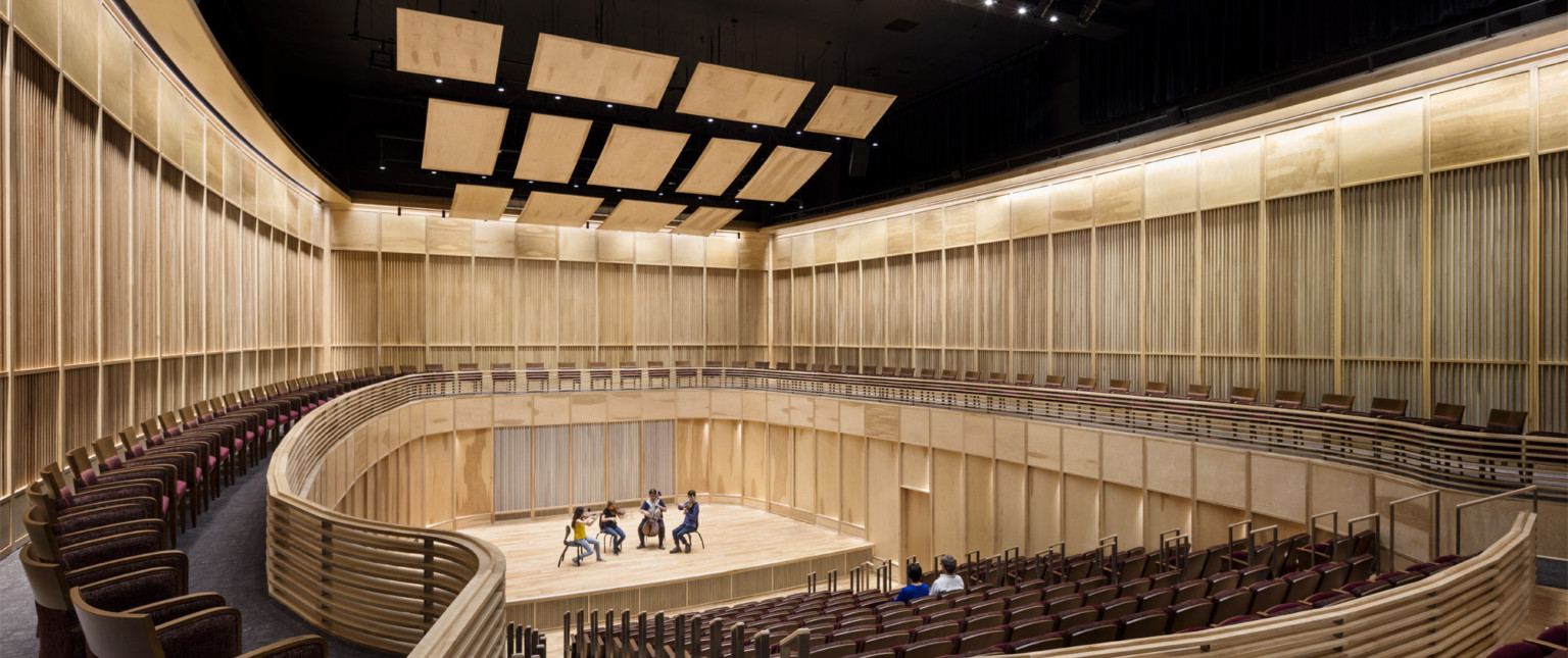 View from the back of wooden wall oval auditorium with 4 musicians on stage and 2 people seated in the audience
