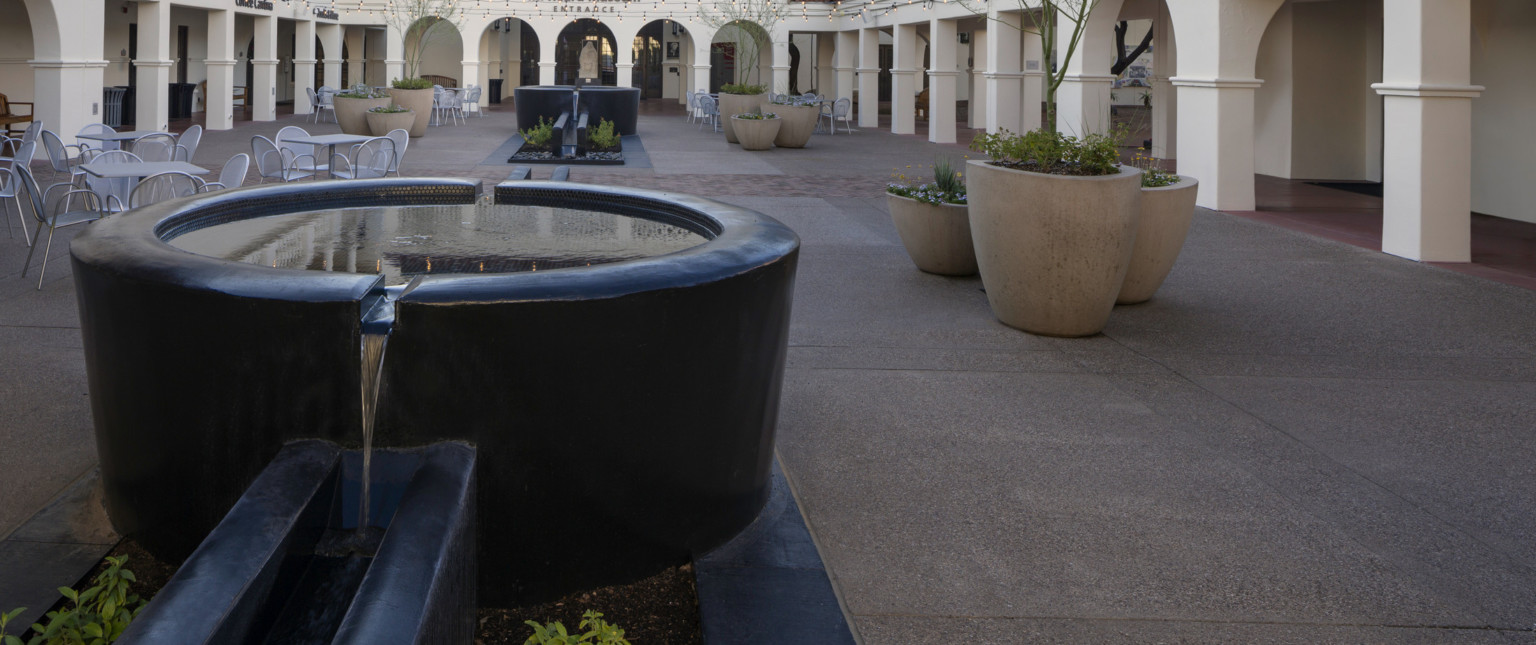 A closeup of a round bowl of a courtyard fountain flowing into one of the long basins below on either side